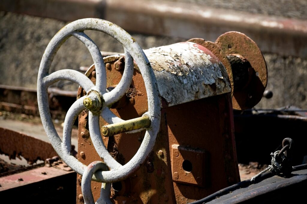 Close-up of a rusty steering wheel on an old industrial machine outdoors.