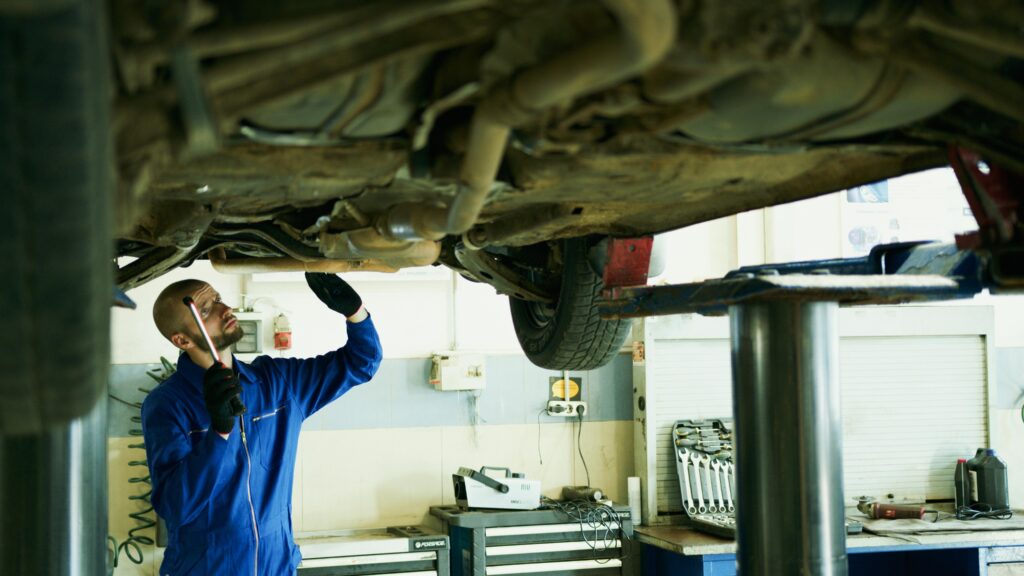 Mechanic inspecting a car's underside in a workshop for repairs.